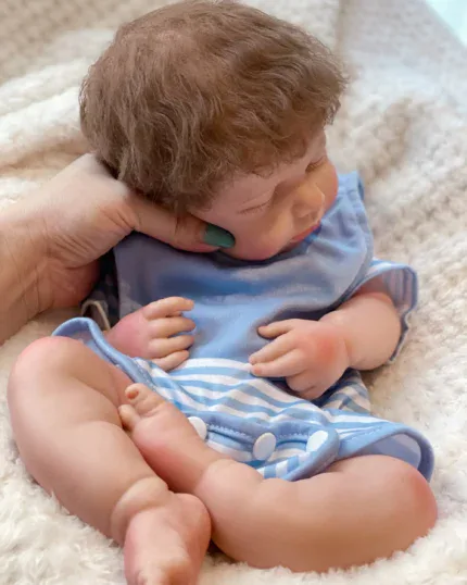 Realistic silicone reborn baby doll with brown hair and blue outfit.