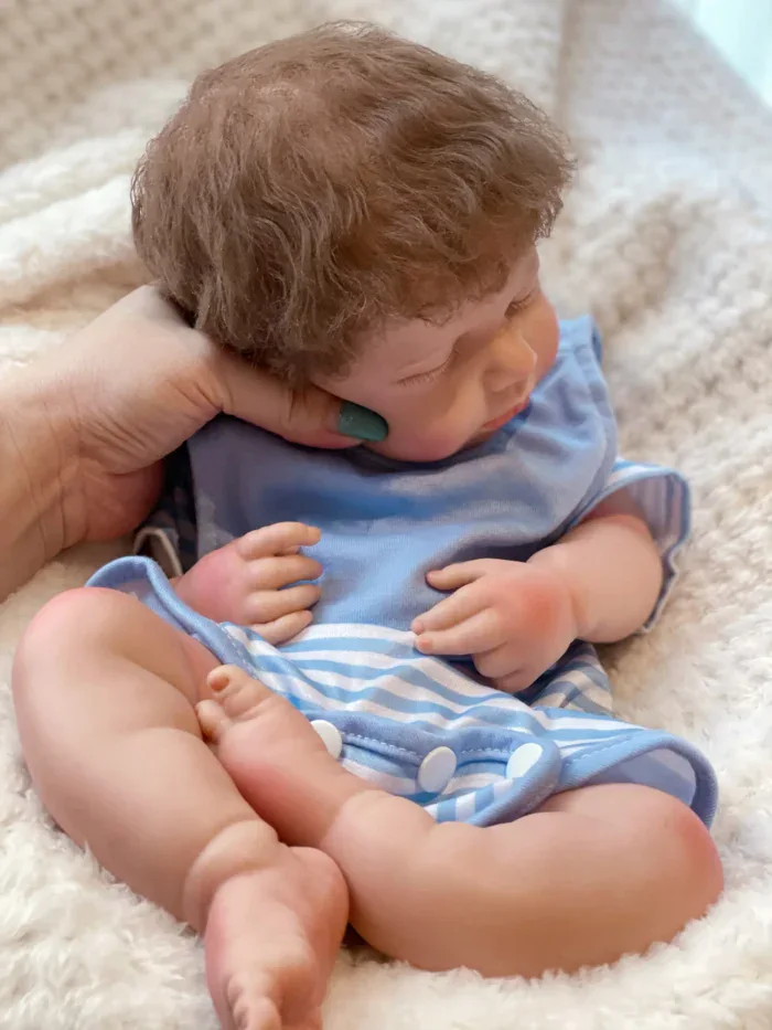 Realistic silicone reborn baby doll with brown hair and blue outfit.