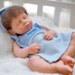 Close-up of a sleeping silicone reborn baby doll in blue outfit.
