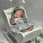 Реалистична преродена кукла бебе, спяща в бяла люлка със сиво одеяло и суичър с качулка.