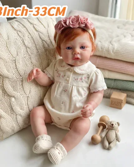 13-inch red-haired silicone reborn doll with pink headband and baby accessories.