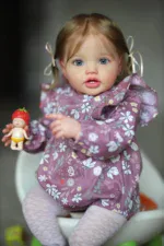 Adorable toddler girl holding a strawberry doll, wearing a floral purple dress.