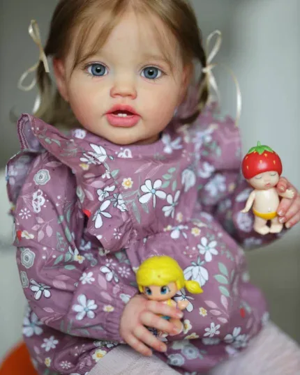 Realistic toddler girl doll with blue eyes and light brown hair holding toys.