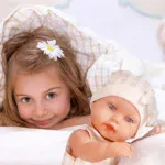 Adorable girl with a doll, both with bright eyes, lying on a bed.