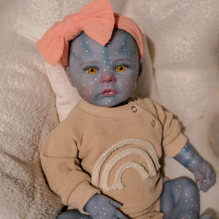 Blue-skinned reborn doll with yellow eyes, pink bow, and rainbow sweater.