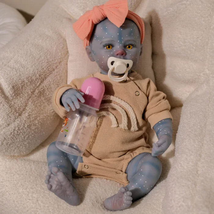 Blue-skinned girl doll with pacifier and pink headband, sitting on plush blanket.