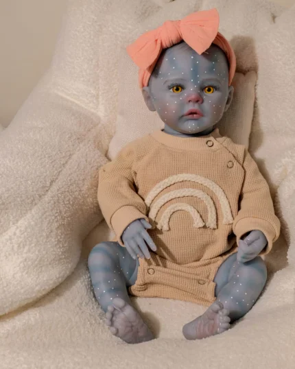 Blue-skinned girl reborn doll with yellow eyes and pink bow, sitting on cream blanket.