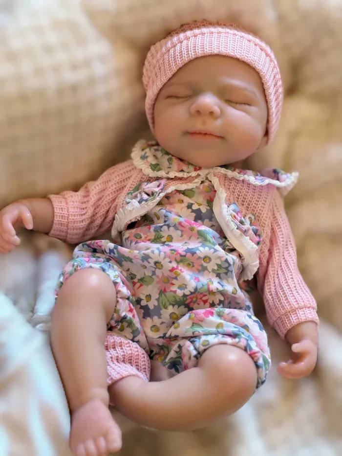 Adorable sleeping baby girl doll with pink hat and floral outfit.