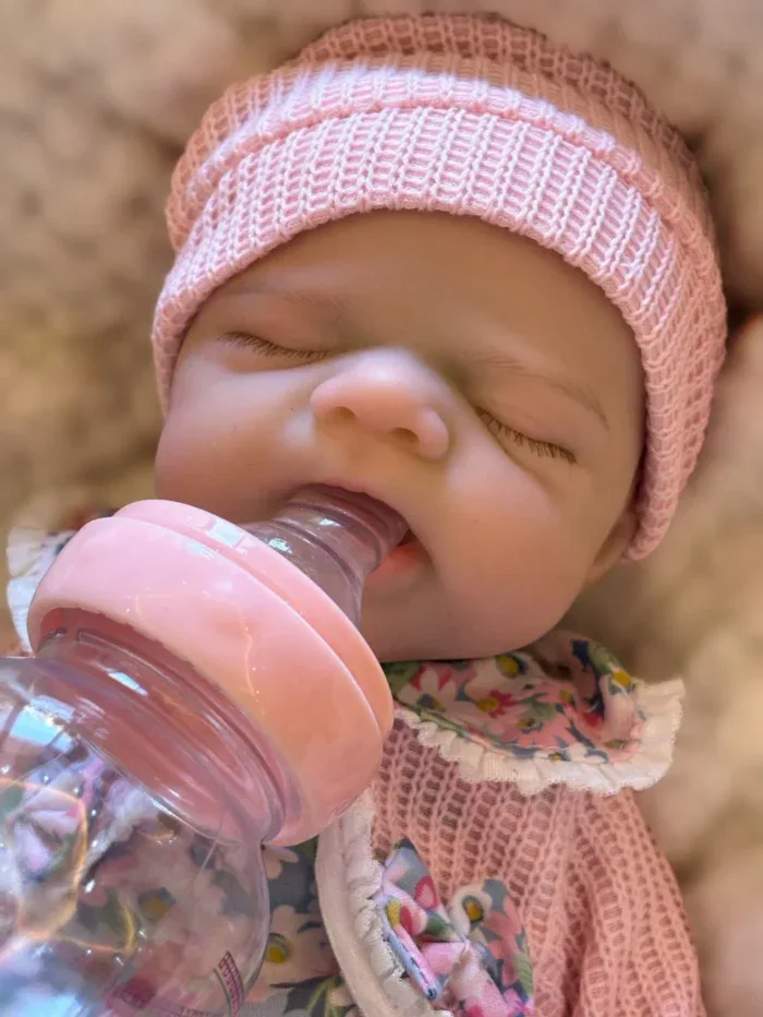 Close-up of a sleeping baby girl with a pink hat and bottle.