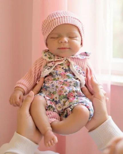 Adorable 13-inch silicone reborn doll of a sleeping baby girl with pink hat and floral outfit.