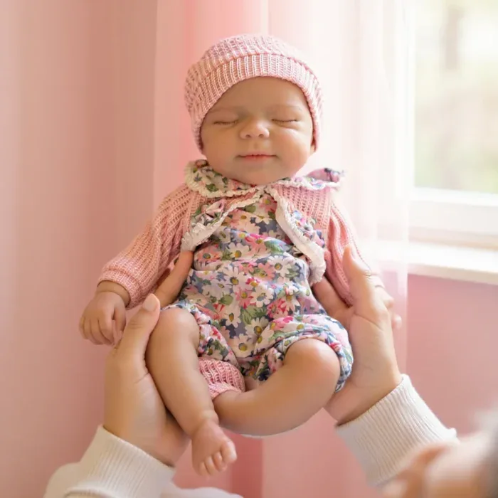 Adorable 13-inch silicone reborn doll of a sleeping baby girl with pink hat and floral outfit.