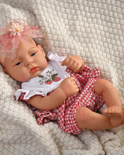Reborn baby doll wearing a red and white checkered outfit with a pink bow headband.