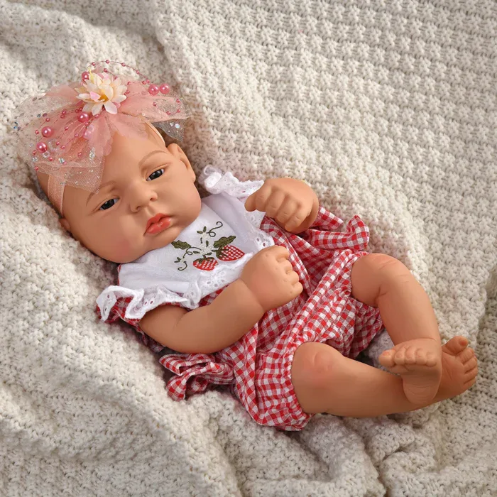Reborn baby doll wearing a red and white checkered outfit with a pink bow headband.