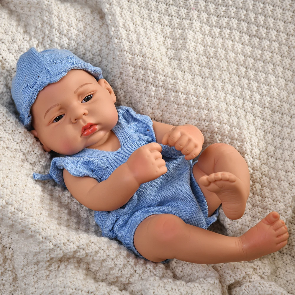 16 Inch Reborn Clothes Sweater Jumpsuit and Pinafore Set 88 Reborn baby doll wearing blue clothes and hat, lying on a cozy blanket.