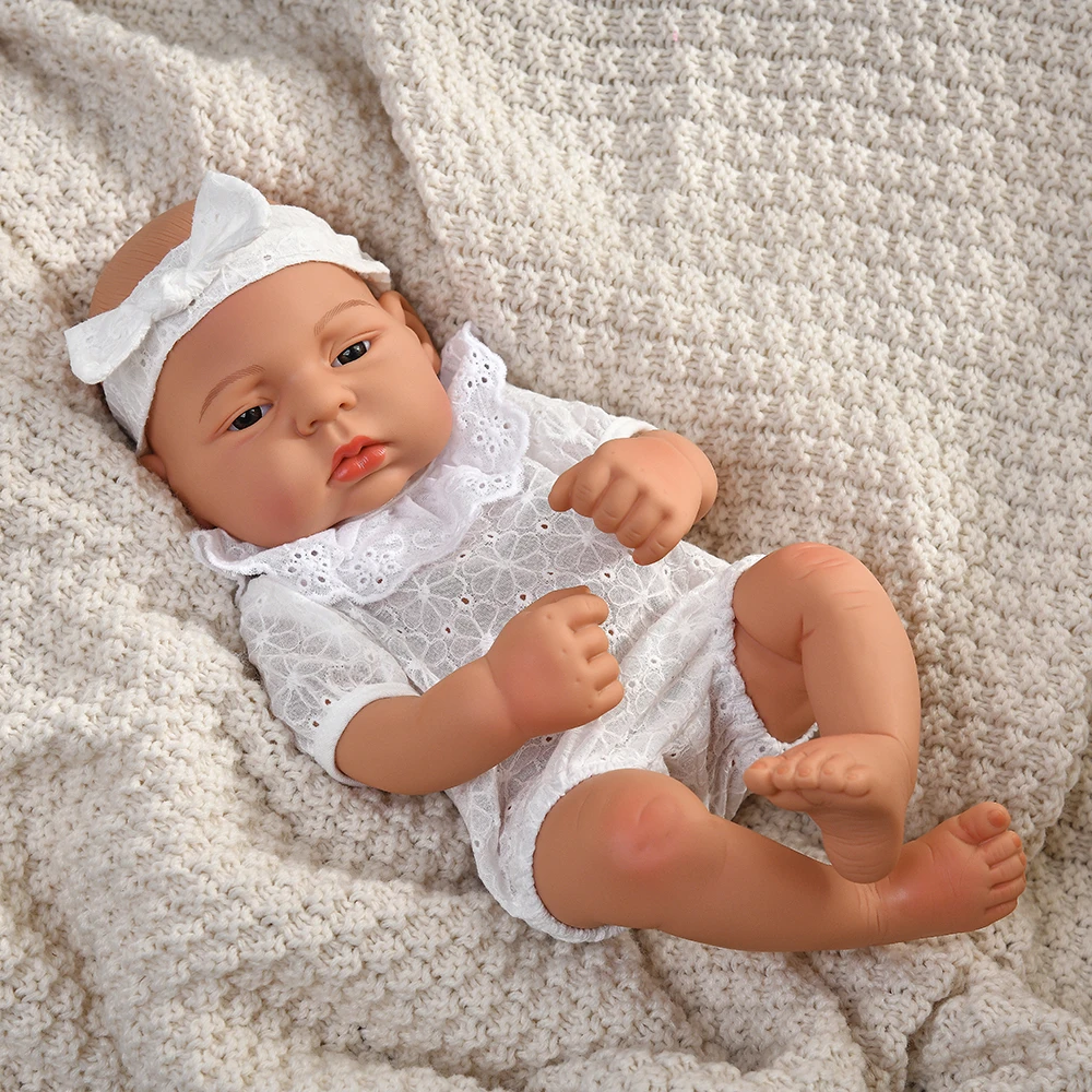 16 Inch Reborn Clothes Sweater Jumpsuit and Pinafore Set 74 Reborn baby doll wearing a white dress and headband on a cozy blanket.