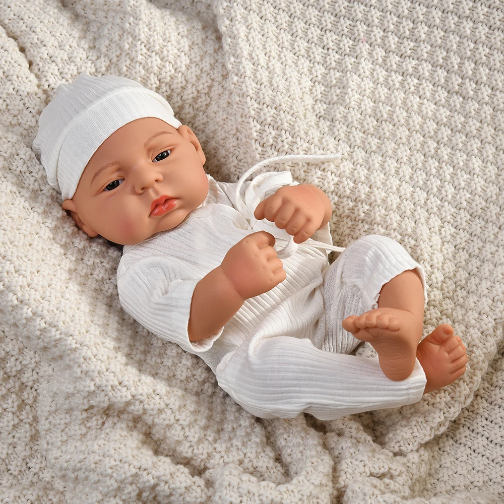 16 Inch Reborn Clothes Sweater Jumpsuit and Pinafore Set 80 Reborn baby doll wearing white clothes and hat on cozy blanket.
