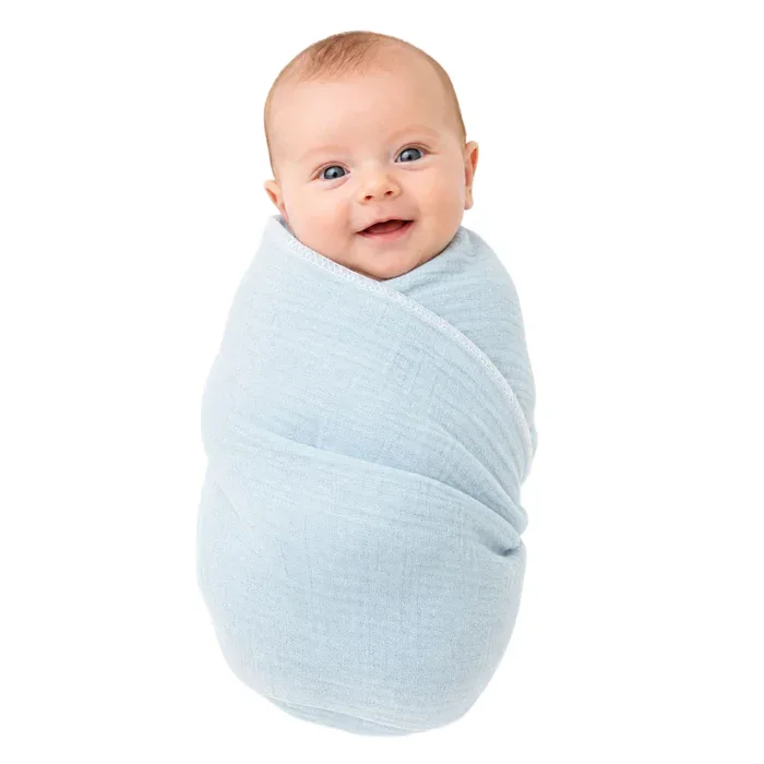 Baby wrapped in light blue cotton gauze blanket, smiling and looking at the camera.