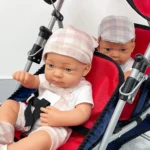 Twin baby dolls in a red double stroller with hats and casual clothes.
