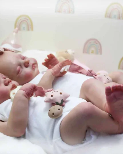 Zwei Zwillings-Reborn-Babypuppen schlafen auf einem Bett mit Regenbogentapete.