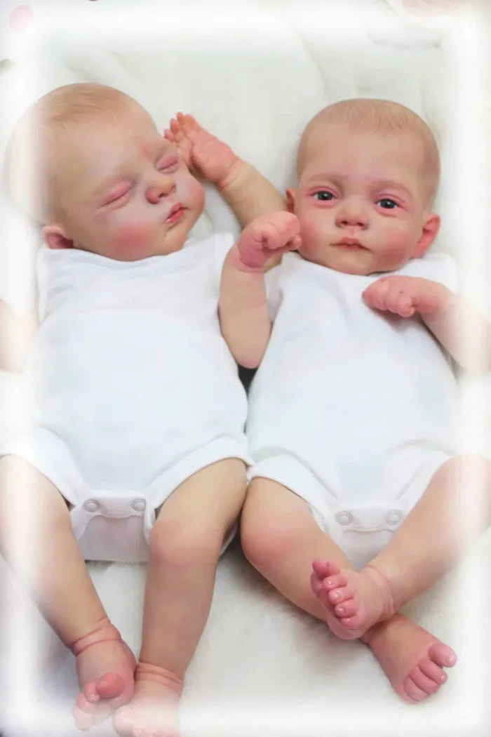 Zwei realistische Zwillingsbabypuppen, schlafend und wach, in weißen Outfits.
