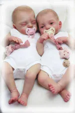Zwei realistische Zwillingsbabypuppen mit Schnullern und passender Kleidung.