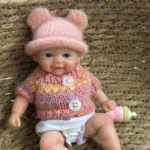 Entzückende, pummelige Reborn-Babypuppe mit rosa Mütze und Pullover.