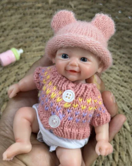 Entzückende, pummelige Babypuppe mit rosa Mütze und Strickpullover.