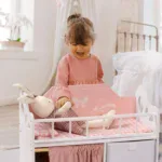 Young girl playing with a pink wooden doll crib and stuffed bunny.