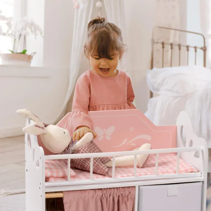 Young girl playing with a pink wooden doll crib and stuffed bunny.