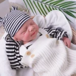 Realistische Silikon-Reborn-Babypuppe (Junge) mit gestreifter Mütze und kuscheliger Kleidung.
