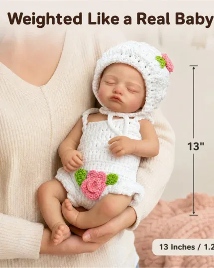 Reborn silicone baby doll in white knit outfit held gently.